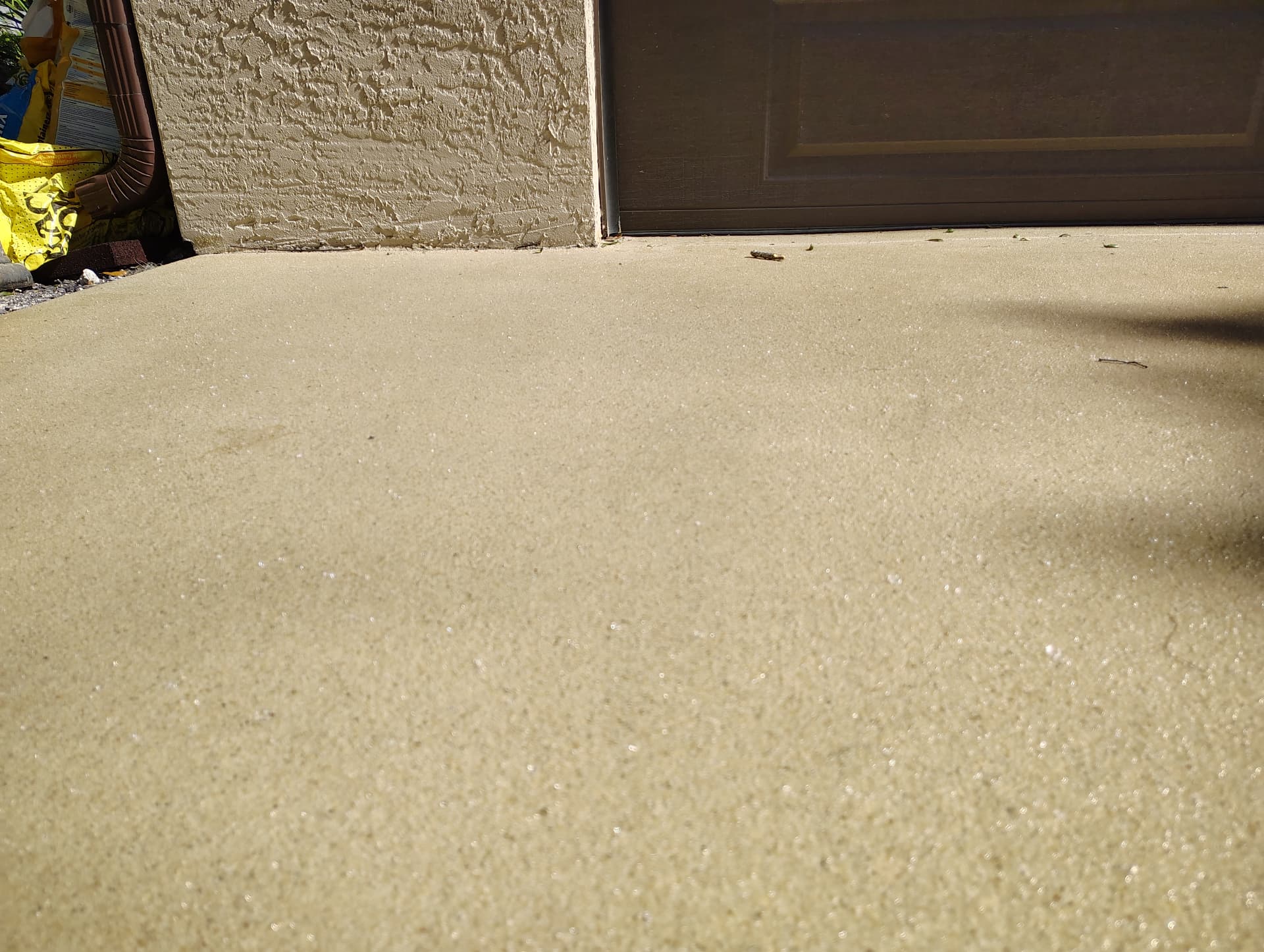 Tan quartz-textured epoxy coating beside a residential garage door