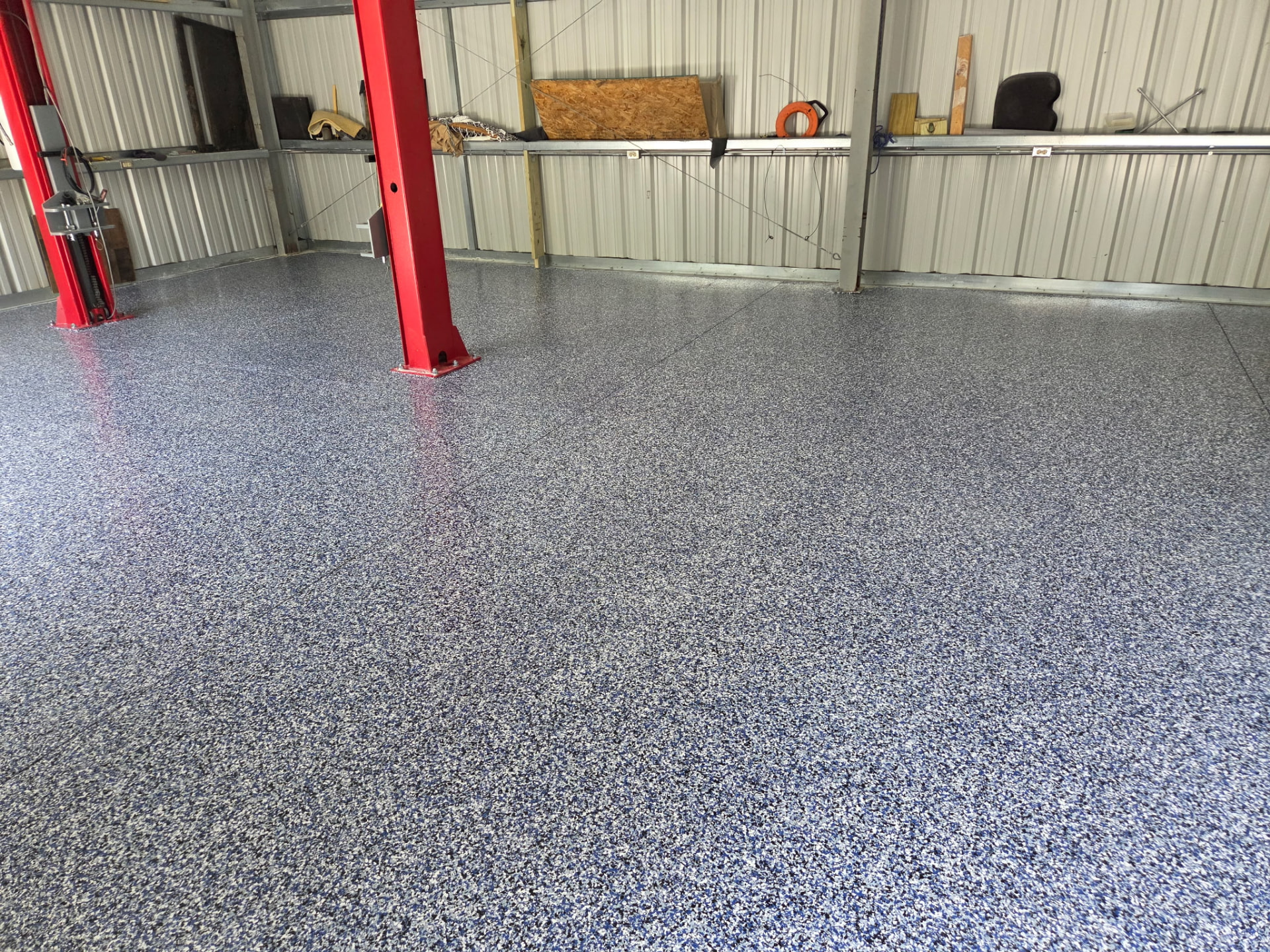 Large workshop floor coated with blue and gray epoxy flake around vehicle lift posts